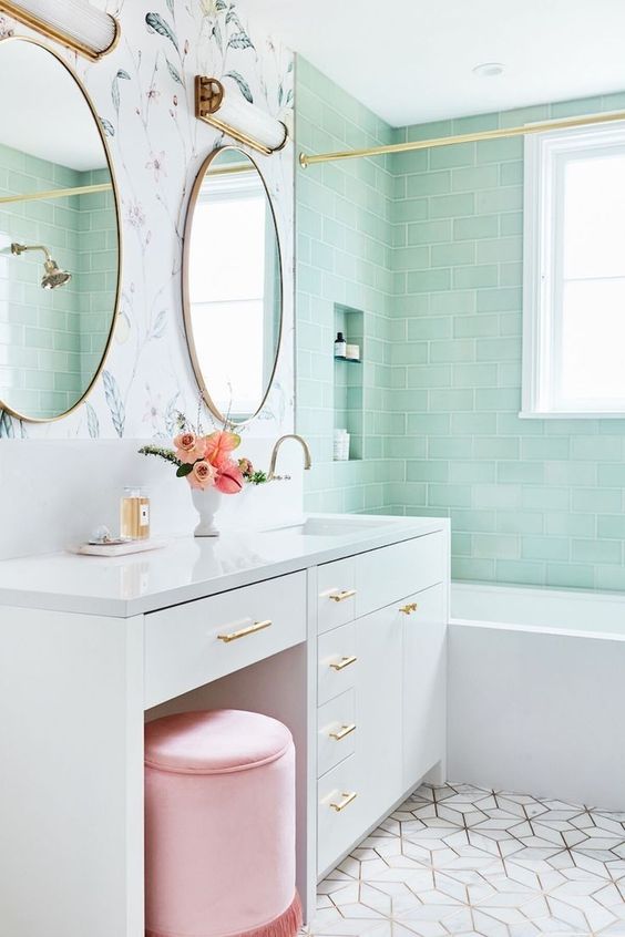 a chic bathroom with mint subway tiles in the bathtub space, a white vanity, a pink pouf and some gold touches for a more glam look