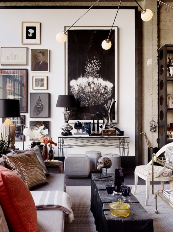 a dramatic living room with a grey sofa, a printed chair, a chest coffee table, bold pillows, a tall gallery wall and a chandelier