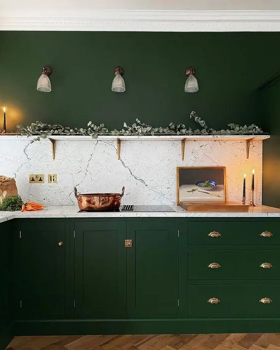 a hunter green kitchen with vintage cabinets, gold handles, an open shelf with greenery and a white stone backsplash