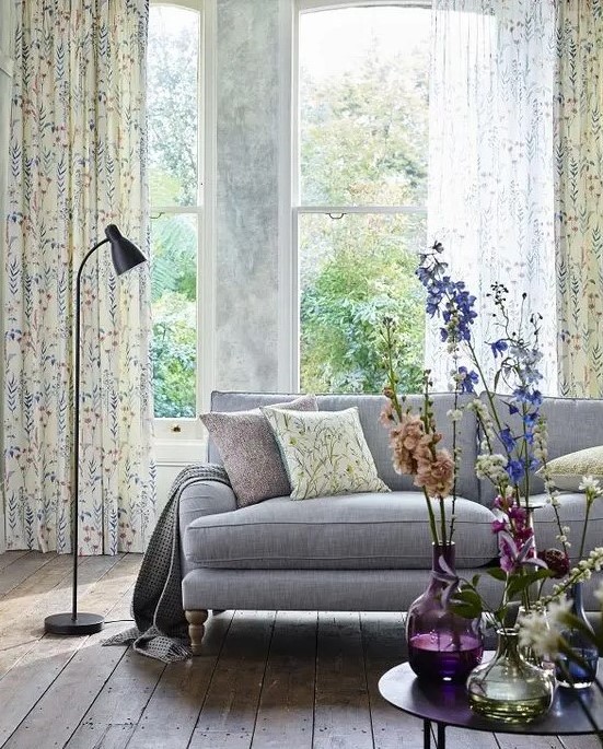 a light and airy spring living room with a grey sofa, floral curtains and fresh blooms in colorful vases is very cool