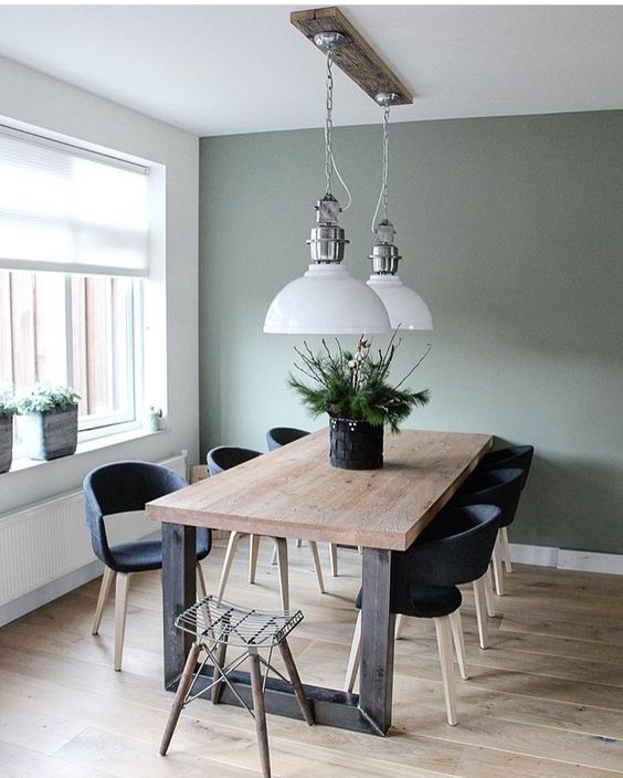 a Scandinavian dining room with a sage green accent wall, a stained table and black chairs, pendant lamps