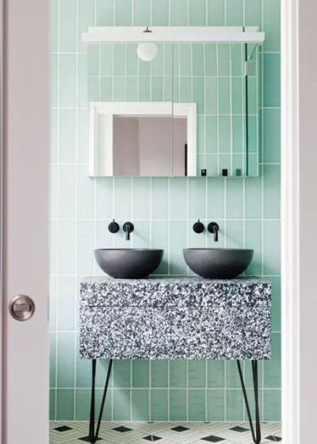 a cool and bright bathroom clad with mint skinny tiles, a terrazzo vanity, black sinks and a mirror cabinet is awesome