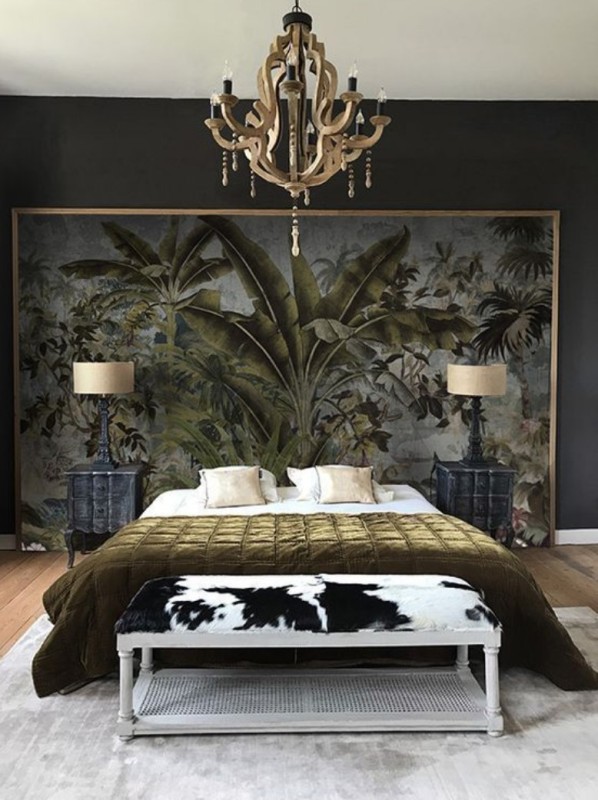 a moody bedroom with a black accent wall, a bed and black nightstands, an upholstered bench, a large scale artwork and a refined chandelier