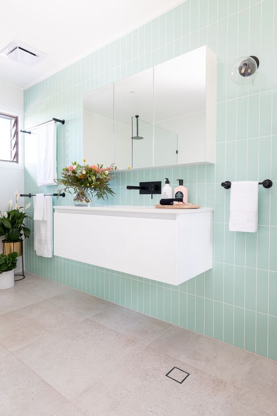 a cool modern bathroom with mint skinny tiles, a white floating vanity, a mirror cabinet and black fixtures for an edgy feel