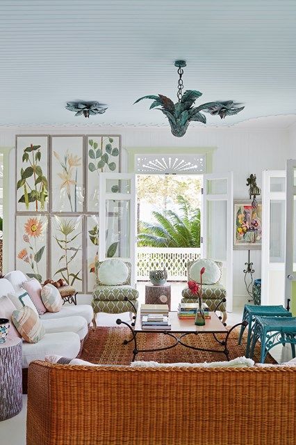 a pretty and eye-catchy living room with a white sofa and a woven sofa, turquoise chairs, a coffee table, printed chairs and a floral print wall