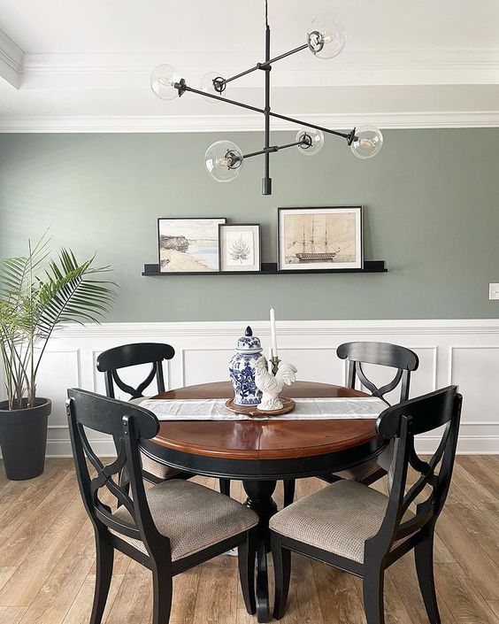 a stylish modern dining room with a sage green wall and paneling, a dark-stained table and chairs, a cool chandelier and some art