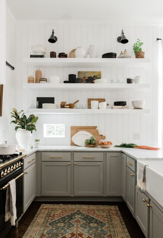 a pretty U-shaped kitchen with grey shaker style cabinets, white countertops, white floating shelves and brass and gold touches for elegance