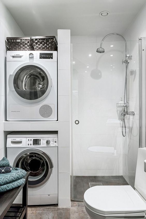 a small minimal bathroom with a washing machine and a dryer, a shower space, a white toilet and a black shelving unit