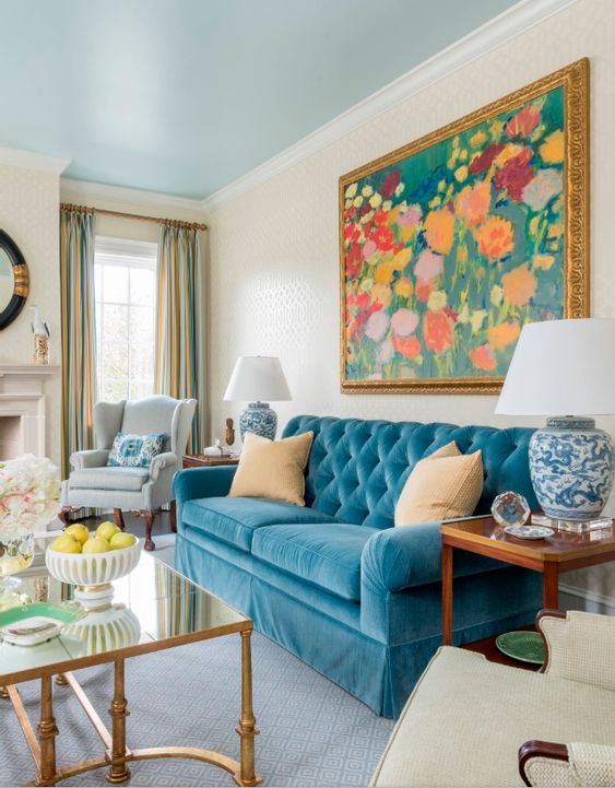 a vintage-inspired living room in neutrals, with a blue sofa, a colorful floral artwork, blue lamps and coffee tables
