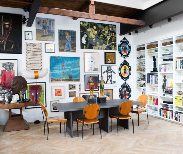 a white dining space with a double-height ceiling and a wall taken by wall art, a grey table and amber chairs