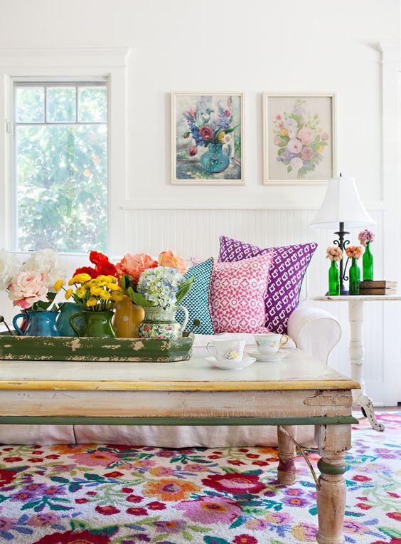 a white living room with a bold floral rug that makes a statement, a white sofa, floral artwork and blooms in vases