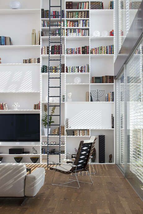 a contemporary living room with a large bookcase that takes a whole wall, neutral seating furniture and a tall ladder is amazing