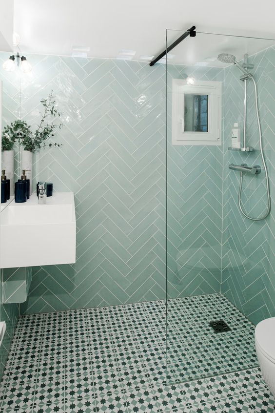 a small bathroom with mint herrignbone tiles and printed ones on the floor, a white floating vanity and black touches