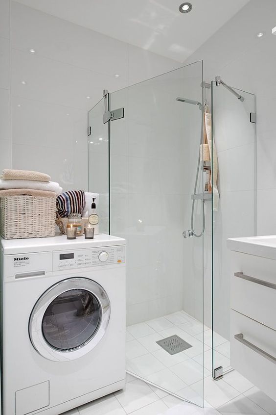 a small white bathroom with a glass-enclosed shower in the corner, a floating vanity, a washing machine and some pretty decor
