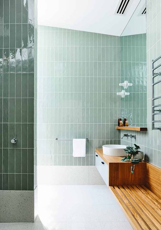 a stylish mint green bathroom clad with skinny tiles, with a floating wooden vanity and a round sink, a potted plant
