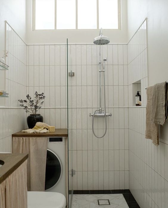 a tiny black and white bathroom with skinny white tiles and black and white ones, a small shower space, a washing machine with a curtain