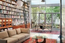 40 a home library with a double height ceiling and a whole wall taken by a bookcase, a desk by the glazed wall and a reading zone with a sofa