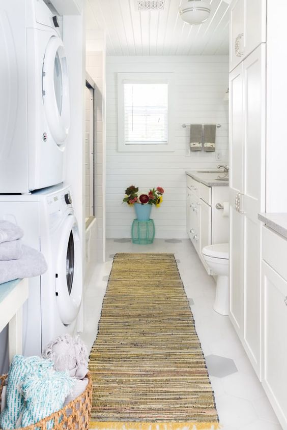 a white farmhouse bathroom clad with beadboard, with a large vanity, a bathtub and a stacked washing machine and a dryer
