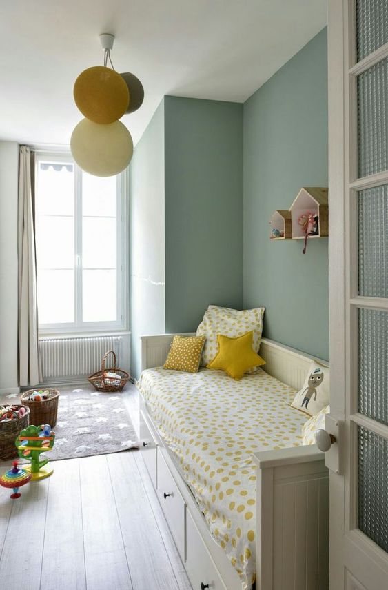 a chic sage green kids' room with a storage bed and bright bedding, baskets with toys and house-shaped shelves