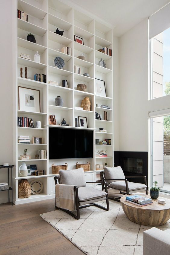 a neutral living room with a double-height bookcase, neutral seating furniture, a wooden coffee table and lots of natural light