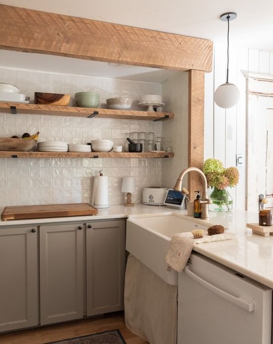 a taupe kitchen with open shelves instead of upper cabinets, white tiles on the backsplash and a vintage sink plus wooden beams