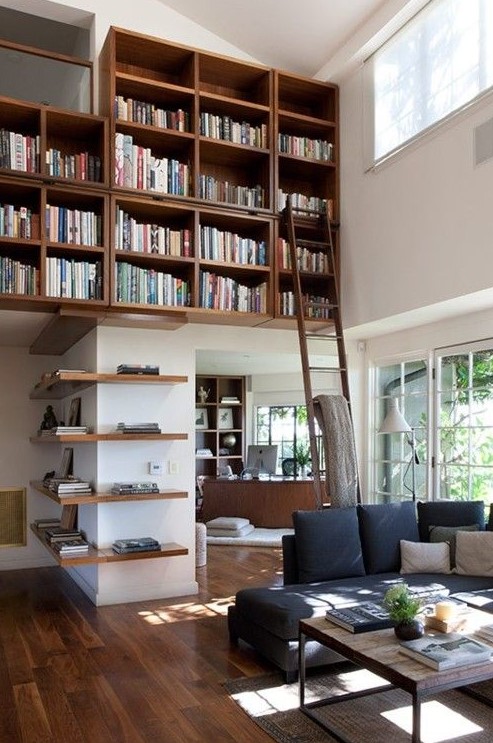 a neutral living room with a large bookcase and bookshelves over the walls, a navy sofa with pillows, a coffee table and lots of natural light
