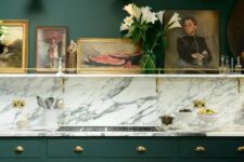 44 a vintage hunter green kitchen with a white marble backsplash and countertops, a shelf with artworks is chic