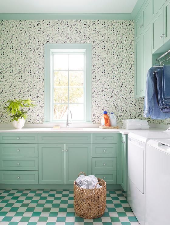 a mint green farmhouse laundry with shaker cabinets, white countertops, printed wallpaper, a green and white checked floor