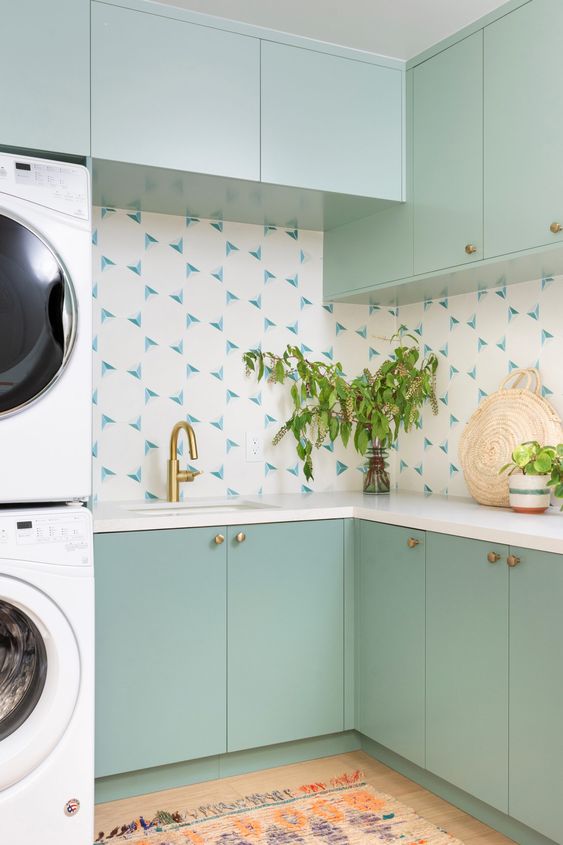 a mint green laundry room with a catchy backsplash, gold fixtures and stacked appliances is a cool space