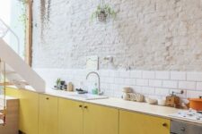 52 a bold contemporary kitchen with yellow plywood cabinets, neutral countertops, a white subway tile backsplash and a brick wall