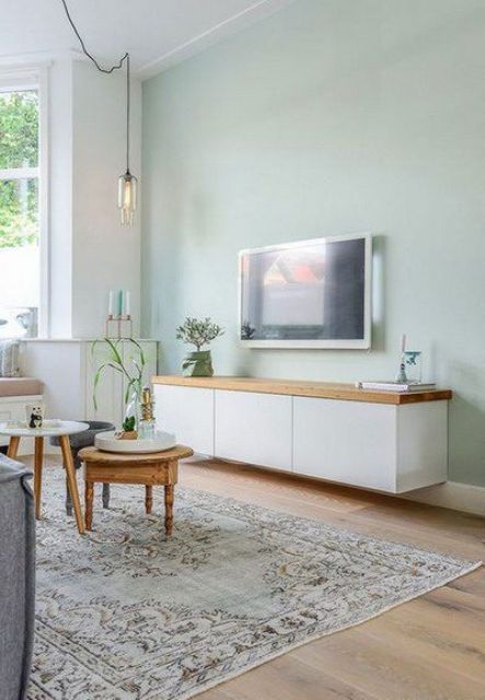 a Scandinavian living room with a mint green accent wall, a grey sofa, a couple of mismatching tables, a floating TV unit