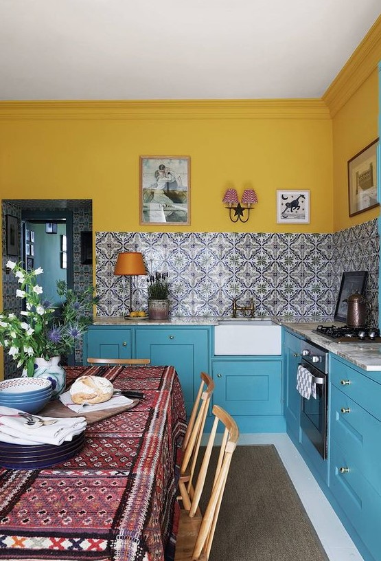 a bright kitchen with yellow walls, blue cabinets, a stone countertops and a beautiful printed tile backsplash for a bolder touch