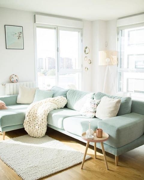 a Scandinavian living room with a mint green sectional, neutral and mint pillows, a knit blanket, a side table and a floor lamp