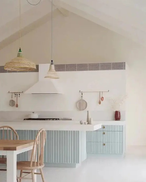 a coastal kitchen with pale blue ridged cabinets and a kitchen island, woven pendant lamps and a white hood that matches the backsplash