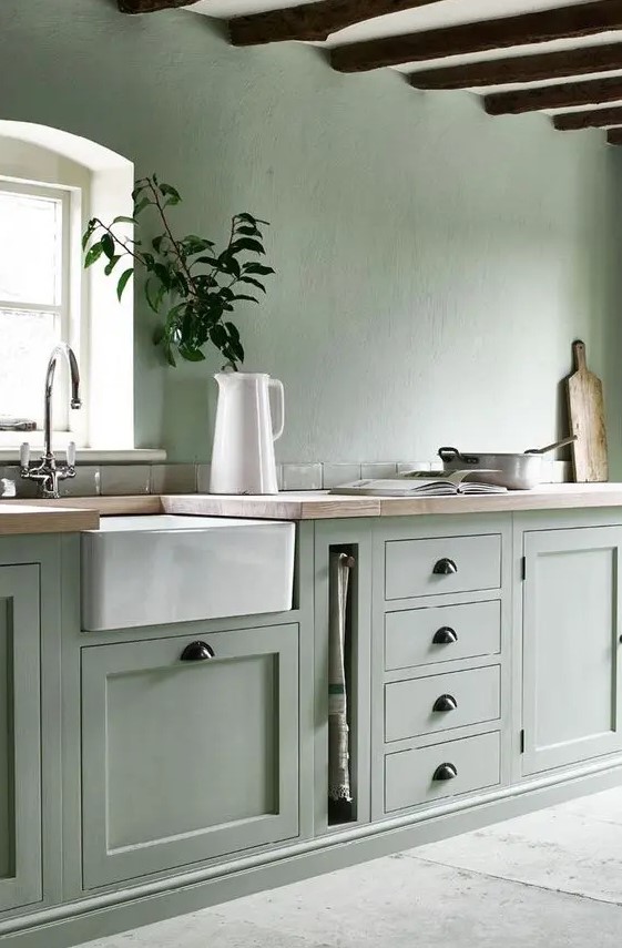 a sage green kitchen with matching walls and cabinetry, wooden beams on the ceiling and wooden countertops plus dark handles