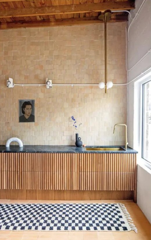 an eye-catchy kitchen with flated lower cabients and a black marble countertop, a tan and beige Zellige tile wall and some art