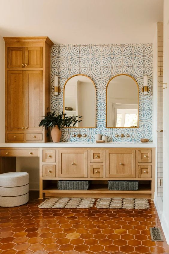 a Mediterranean bathroom with blue printed tiles, a terracotta tile floor, stained cabinets and arched mirrors