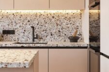 a beautiful blush kitchen with pretty neutral terrazzo countertops and a backsplash plus built-in lights and black fixutres