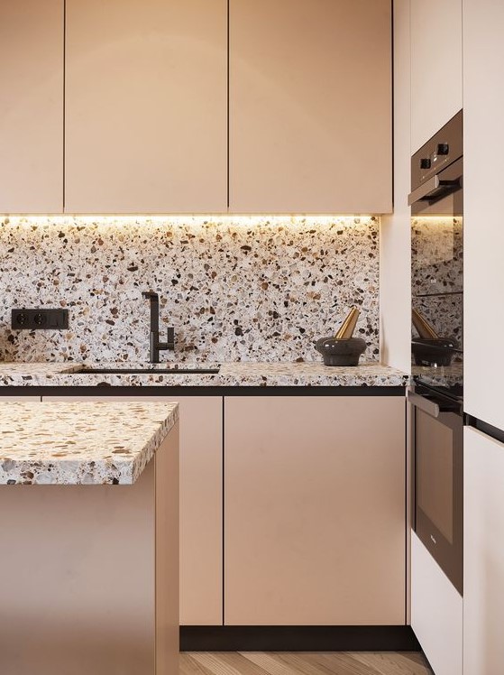 a beautiful blush kitchen with pretty neutral terrazzo countertops and a backsplash plus built in lights and black fixutres