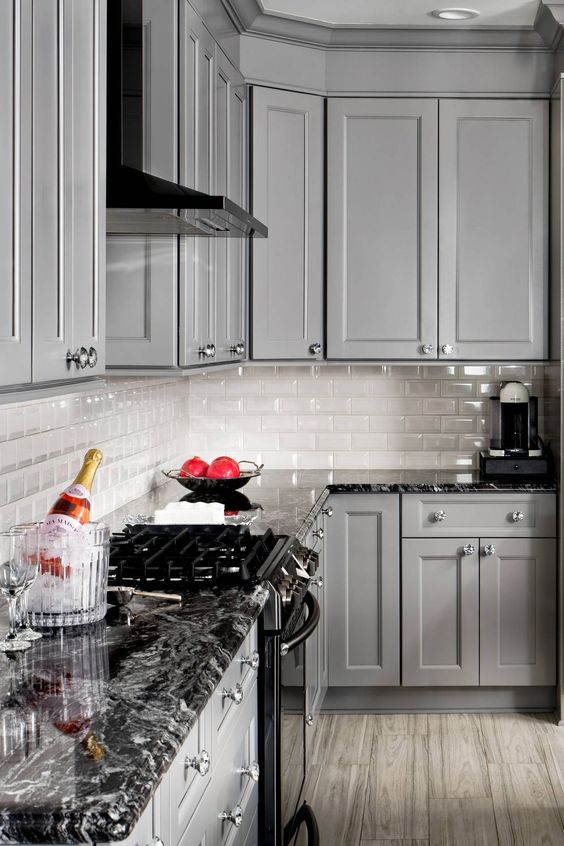a beautiful grey kitchen with shaker cabinets, a white tile backsplash, black granite countertops and black appliances