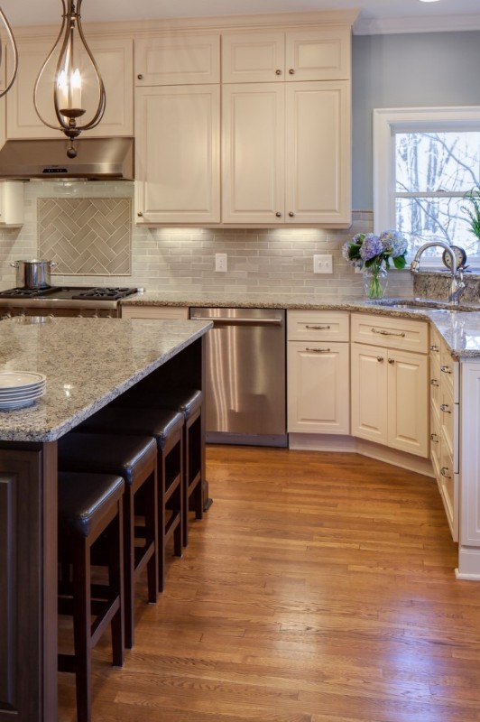 a beautiful kitchen with creamy shaker cabinets, a rich-stained kitchen cabinet and stools, a creamy tile backsplash and grey granite countertops