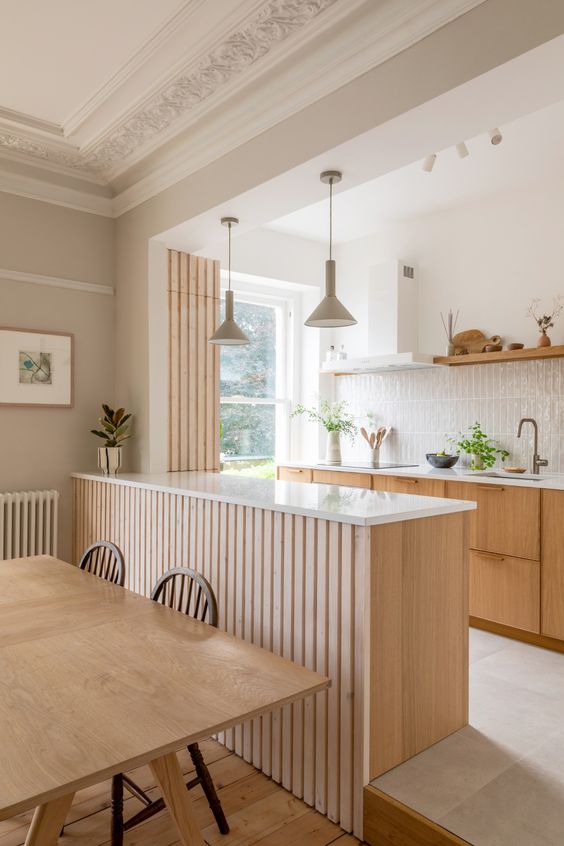 a beautiful light-stained flat panel kitchen with a glossy white tile backsplash, a fluted kitchen island and white pendant lamps