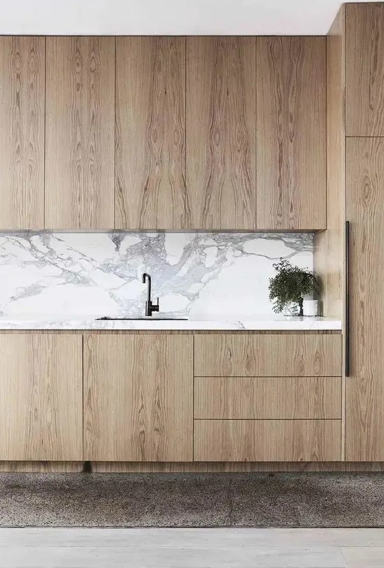 a beautiful light stained kitchen with sleek cabinets, a white stone backsplash and countertops, black fixtures is chic