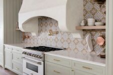 a beautiful modern Mediterranean kitchen with shaker cabinets in sage green, white stone countertops and a bold printed tile backsplash