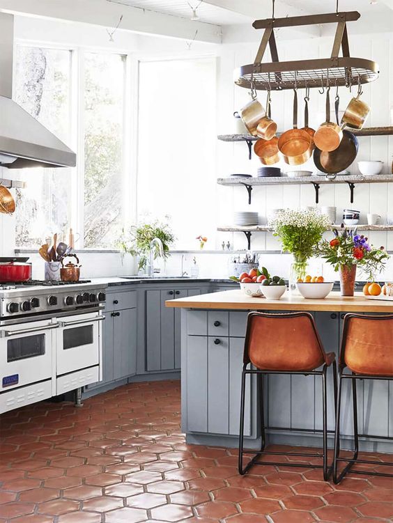 a beautiful rustic kitchen with lots of natural light, shiplap walls, a terracotta tile floor, slate grey cabinets, leather stools