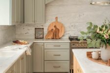 a beautiful shaker style sage green kitchen with white countertops and a backsplash, a stained kitchen island, pendant glass lamps