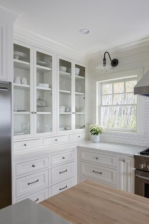 a beautiful white kitchen with inlay and glass cabinets, stainless steel handles and knots, a white subway tile backsplash