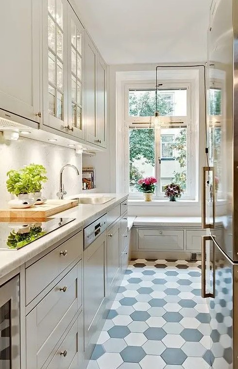 a beautiful white kitchen with white countertops, a white backsplash, shaker and glass front cabinets, a hex tile floor and a windowsill bench