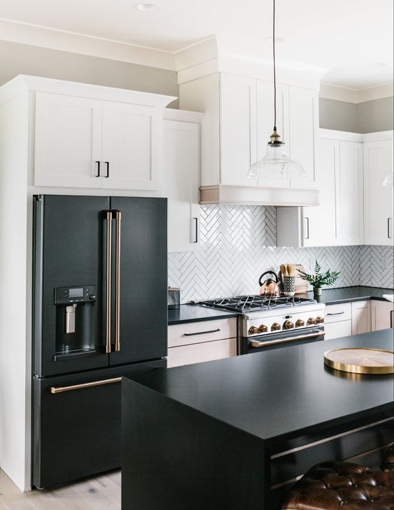 a black and white farmhouse kitchen with shaker cabinets, black soapstone countertops, a white herringbone tile backsplash and pendant lamps