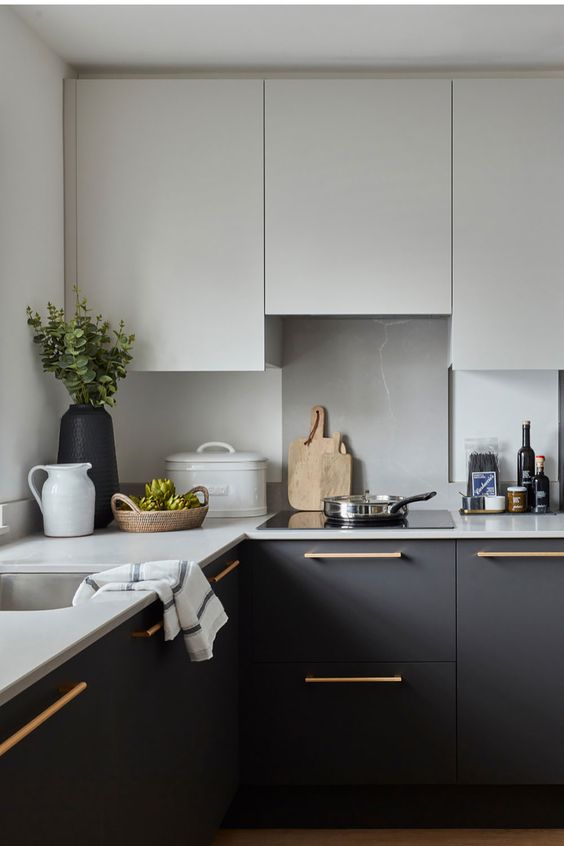 a black and white kitchen with matte flat panel cabinets, a neutral backsplash and white countertops plus gold handles